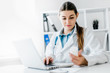 © zadorozhna - Smiling young female doctor working at the clinic , she is using a computer and writing medical reports.