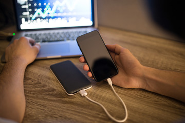 Young developer uses a power bank to charge his mobile phone while working on a project