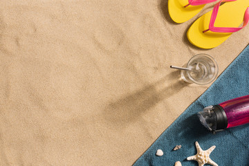 Wall Mural - Summer vacation composition. Flip flops, water bottle and glass of water on sand background. Harsh light with shadows. Summer background. Border composition made of towel