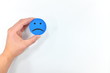 Hand holding a sad emoticon in white background. Sadness and unsatisfied customer concept.