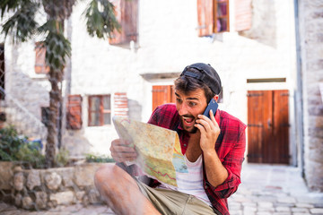 Wall Mural - Handsome beard man talking on phone and using paper map in new town