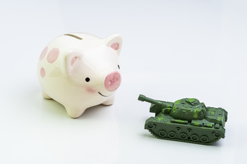 Trade war, economic impact of war or trading power concept, miniature tank toy pointing the gun at smiling pink piggy bank on white background