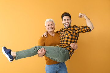 Young man and his father having fun on color background