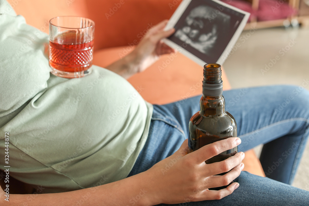 Young pregnant woman drinking alcohol at home