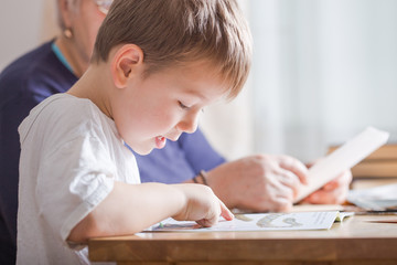 little boy 4 years old reading book. He is sitting on chair  in sunny living room watching pictures in story. Kid doing homework for elementary school or kindergarten. Children study.