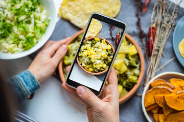 Wall Mural - Take picture of food with phone at kitchen. Smartphone photo of vegetables, potato, cabbage stew. Vegan healthy dietary food.