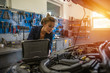 © Dragana Gordic - An attractive woman mechanic working on a car in a repair shop. A female mechanic is working under a bonnet of a car in a garage repair shop. She is wearing blue overalls.