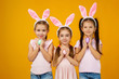 © producer - happy cute little child girls with pink bunny ears holding painted Easter eggs on studio yellow background. Easter day