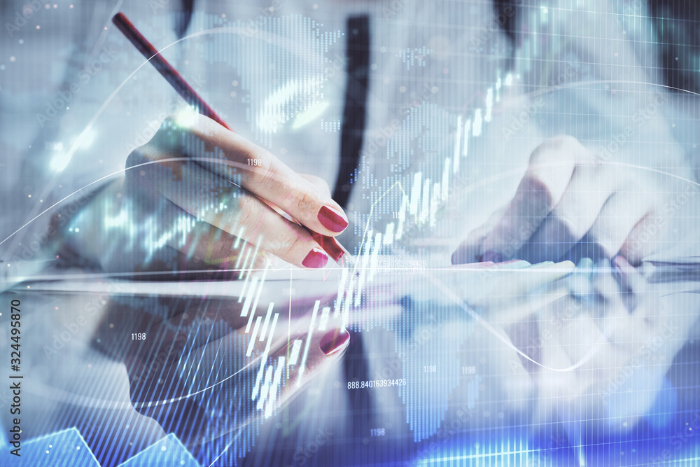 A woman hands writing information about stock market in notepad. Forex chart holograms in front. Concept of research.