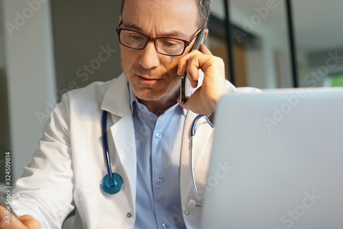 Fotomural Doctor in office working on laptop talking on phone