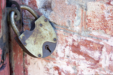 An old padlock on closed doors, a rusty lock on the gate. Brick wall.