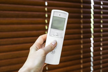 Remote Control For Blinds. Female Hand Holds And Directs A Remote Control On Wooden Shutters To Open It