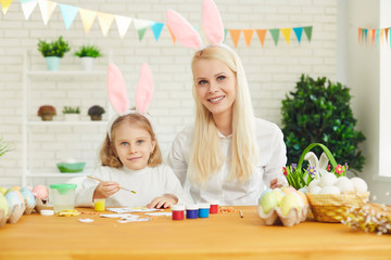 Happy easter. Daughter and mother with rabbit ears decorate Easter eggs sitting at a table