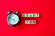 © doucefleur - start now concept with text on wooden block and alarm clock on red background