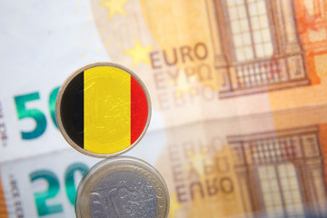 Macro photo of a coin in 1 euro with the Belgian flag on a blurred background banknote in 50 euro. Reflection of the coin on the glass table. Very small depth of field.