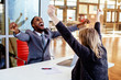 © Carlos David - Portrait of a happy smiling young man in business suit with woman coworker or client celebrating with arms and fists up in office meeting