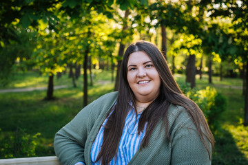 Beautiful and confident brunette smiling plus size model  sitting in the park spring summer day