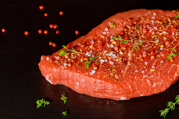 Raw sirloin beef with herb, salt and peppercorn over black stone board.