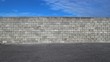 © luca piccini basile - Cinder block wall with an asphalt road in front and blue sky with clouds above it. Background for copy space