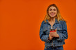 © IC Production - A woman with wavy fair hair in a denim jacket smiles at the camera with a red cardboard cup of coffee in her hands.