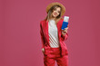 © nazarovsergey - Blonde model in straw hat, white blouse and red pantsuit. She is holding passport and ticket while posing against pink studio background. Close-up