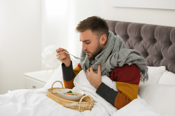 Poster - Sick young man with bowl of tasty soup in bed at home