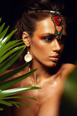 Closeup portrait of woman tanned skin colored makeup tropical jungle paint on the face sweat plant palm leaves wild style exotic accessory beautiful sexy model ethnic model.