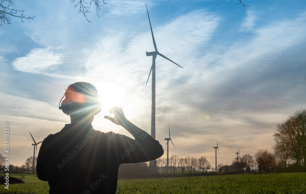 Engineer standing in front of a wind turbine during sunset. - obrazy, fototapety, plakaty 