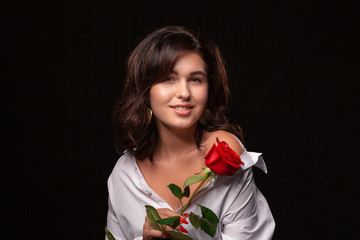 Beautiful woman with bright makeup posing isolated over black background with red rose.