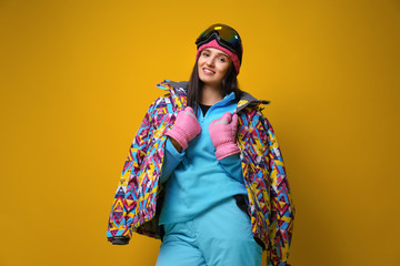 Wall Mural - Woman wearing stylish winter sport clothes on yellow background, low angle view