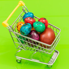 Wall Mural - A shopping cart filled with Easter eggs.  The concept of Holiday shopping and high prices.  Green background, 