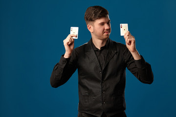 Noob in poker, in black vest and shirt. Holding two playing cards while posing against blue studio background. Gambling, casino. Close-up.