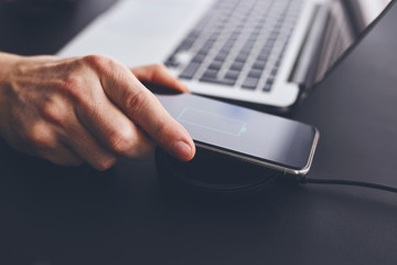 Wall Mural - man charging mobile phone on wireless charger on table