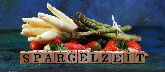 Wall Mural - White and green asparagus with strawberries on rustic background with Spargelzeit wooden letter.