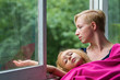 © vkaganovich - Mother and daughter are sitting by the open window during the rain, the mother holds her daughter in a blanket on herself and looks sadly at the rain through the window.