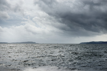 Dramatic stormy sky. A view of the Firth of Clyde from the sailing boat. Forests, hills and mountains of the Bute Island in the background. Scotland, UK