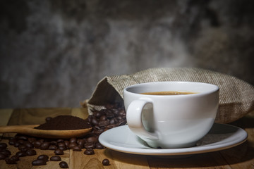 Black coffee in a white mug on a wooden table with roasted coffee beans and a spoon