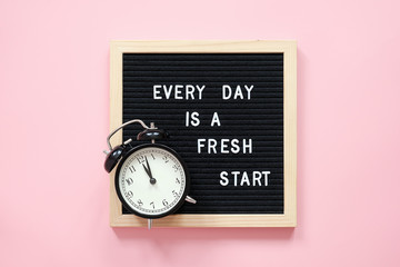 Wall Mural - Every day is a fresh start. Motivational quote on black letter board and black alarm clock on pink background. Concept inspirational quote of the day. Greeting card, postcard