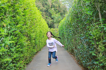 Asian little child girl running in garden Maze. Kid playing in labyrinth for fun and entertainment