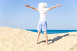 © zabavna - Summer sea vacation. Happy young female arms apart wearing a white hat with a wide brim enjoying life on the sandy beach by the sea on clear sunny day. Back view