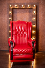 Wall Mural - Old vintage red leather chair in a dark room and a frame with glowing lights in the background. Background for a photo shoot