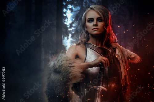 Beautiful warrior woman holding a sword wearing steel cuirass and fur in night forest. Fantasy fashion. Cosplayer as Ciri from The Witcher.