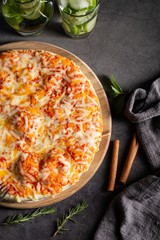 Wall Mural - Vertical overhead shot of a pizza on a black table with mojitos and cinnamon on the side