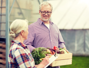 Wall Mural - farming, gardening, agriculture, harvesting and people concept - senior couple with box of vegetables and clipboard at farm greenhouse