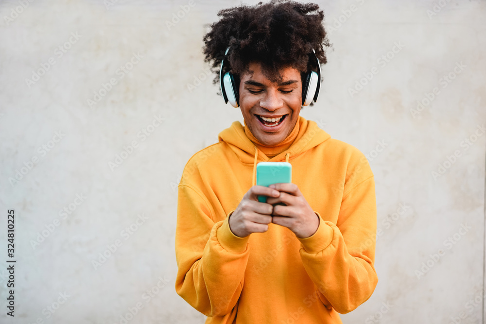 Happy african millennial guy listening music playlist with smartphone app outdoor - Young man having fun with technology trends - Tech, generation z and stylish concept - Focus on face - obrazy, fototapety, plakaty 