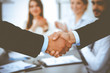 © rogerphoto - Business people shaking hands at meeting while theirs colleagues clapping and applauding. Group of unknown businessmen and women in modern white office. Success teamwork, partnership and handshake