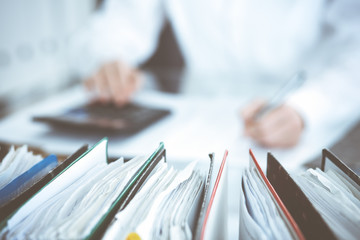 Binders of papers waiting to process by bookkeeper woman or financial inspector, close-up. Business portrait. Audit or tax concepts