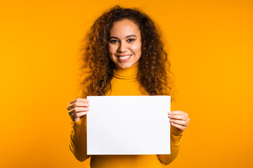 pretty curly woman holding horizontal white a4 paper poster. copy space. smiling trendy girl on yell