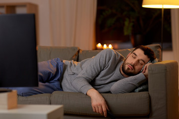 Wall Mural - leisure and people concept - man sleeping on sofa with tv on at home at night