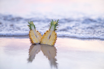 two fresh juicy pieces pineapple on beach, pineapple hits by waves, sunset time, with reflection on sand, yellow exotic fruit. Photo is ideal for advertising, poster and wallpaper